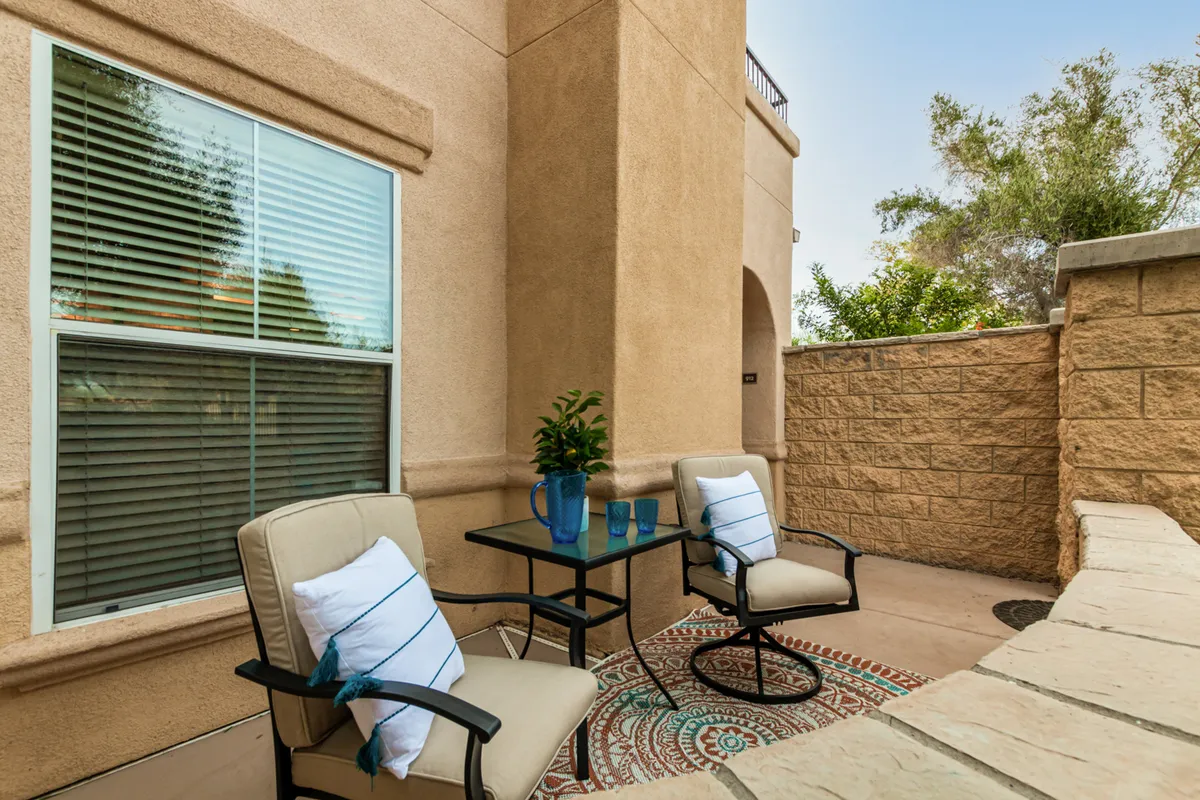 A peaceful patio setup featuring comfortable seating, a decorative table, a green plant, and a colorful rug, creating a tranquil spot for morning coffee, casual meetings, or evening relaxation.