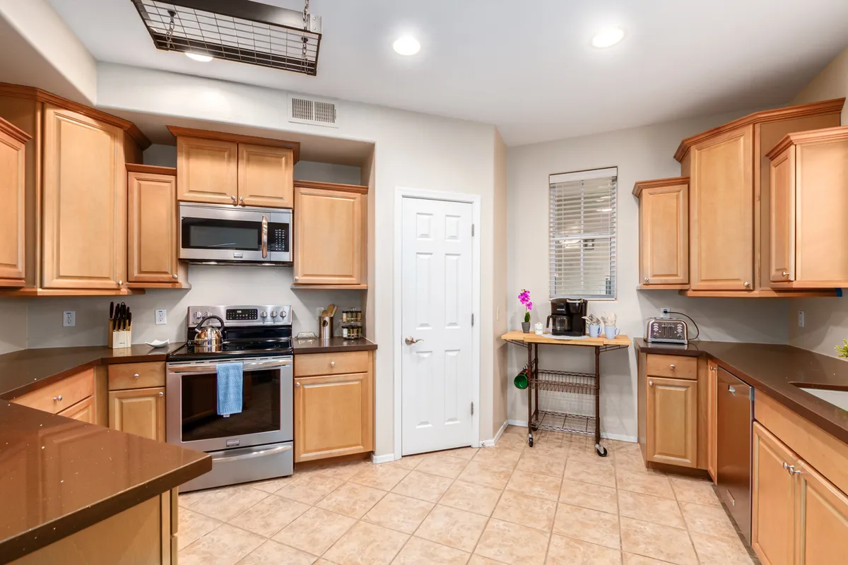 A welcoming, sunlit kitchen featuring a prominent island, stainless steel appliances, granite countertops, and wooden cabinetry. The layout encourages gathering around the island for baking, preparing meals, or enjoying coffee with a friend. The design balances practicality with aesthetic warmth.