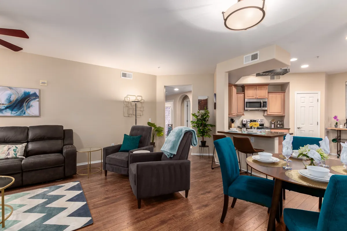 A wide view of the open-concept living space, showcasing a comfortable sofa, a dining table for four, and a stylish kitchen area. Artwork adorns the wall, and the scene is staged for dining, socializing, and relaxing. Natural light fills the space, emphasizing the seamless flow between living, dining, and kitchen zones.