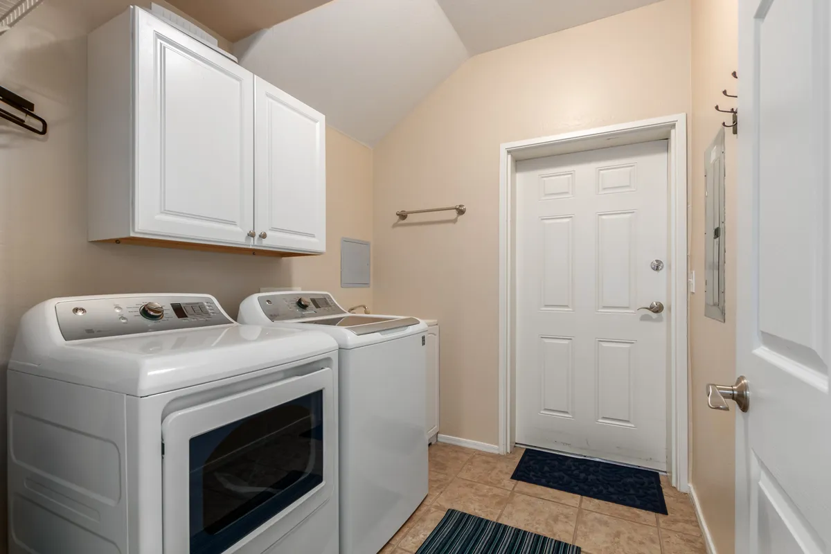 This interior image features a full-size laundry room setup, with a washing machine and dryer side by side, ample storage cabinets above, and a doorway offering a glimpse into an adjoining space. The area is clean, organized, and practical, emphasizing convenience for longer stays.