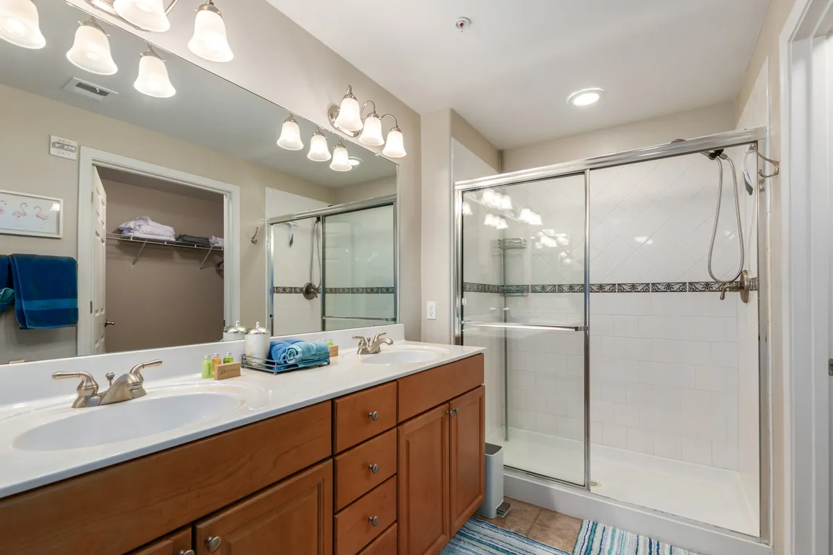 A modern, spa-like bathroom featuring dual sinks, a large mirror, glass shower enclosure, and elegant lighting. The fresh, invigorating ambiance is perfect for morning routines or winding down in the evening.