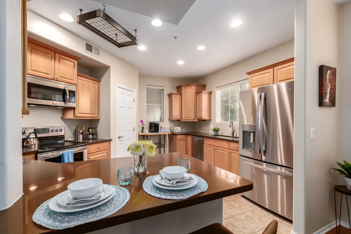 A bright, cheerful kitchen featuring a spacious island, gleaming stainless steel appliances, and an abundance of wooden cabinetry. The large counters provide ample prep space, while the open layout allows for easy movement and social interaction. The overall ambiance is lively and inviting, ideal for cooking or entertaining guests.